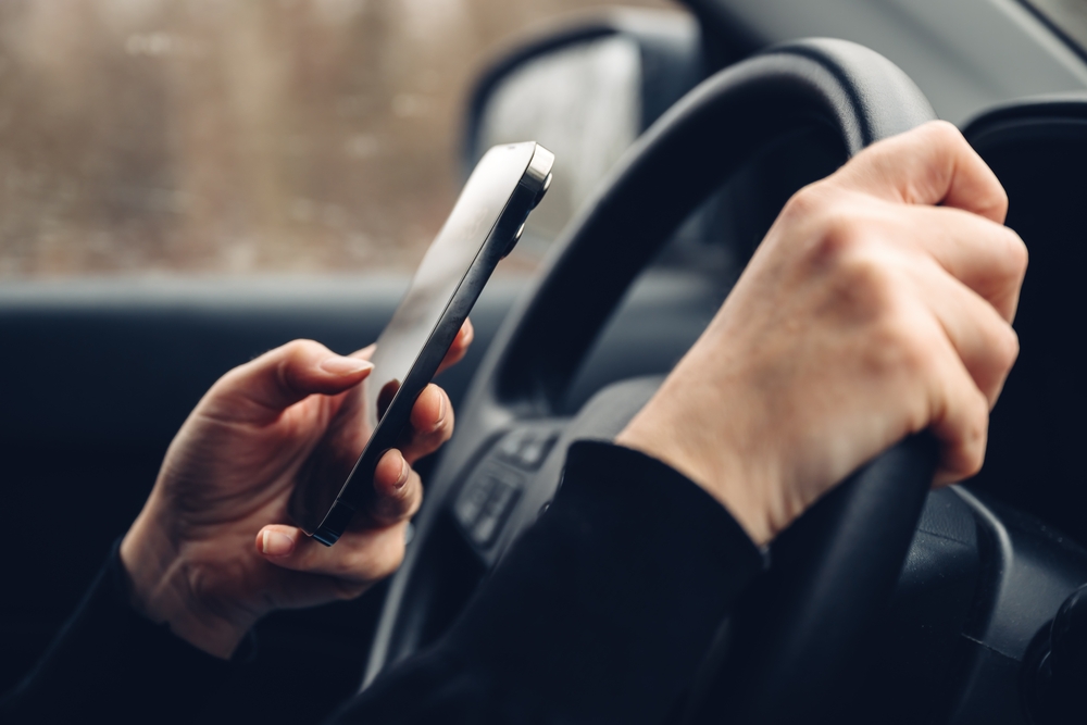 Closeup of female hands typing text message on cell phone while driving car