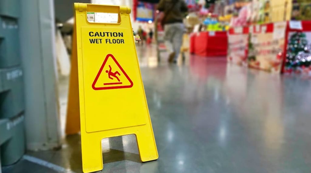 Yellow "Caution Wet Floor" sign in a store with a reflective, possibly wet, floor.