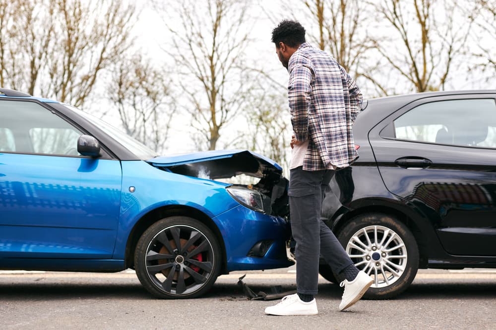 Young man examines rear-end damage after car accident.