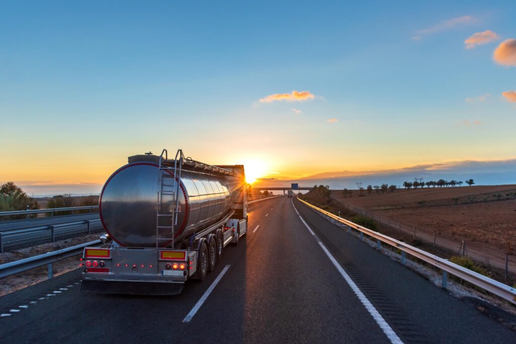 A silver tanker truck driving on an open highway at sunset highlights the dangers of tanker truck accidents in Bakersfield and Kern County.