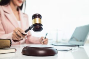 Female lawyer in a pink suit holding a gavel in a courtroom setting, symbolizing legal judgment and decision-making.