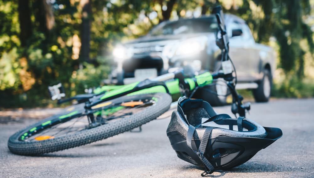 Close-up of a bicycling helmet fallen on the asphalt next to a bicycle after car accident on the road.