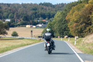 Motorcyclist riding on a rural road in Bucks County, surrounded by fields and trees, symbolizing motorcycle travel and road safety.