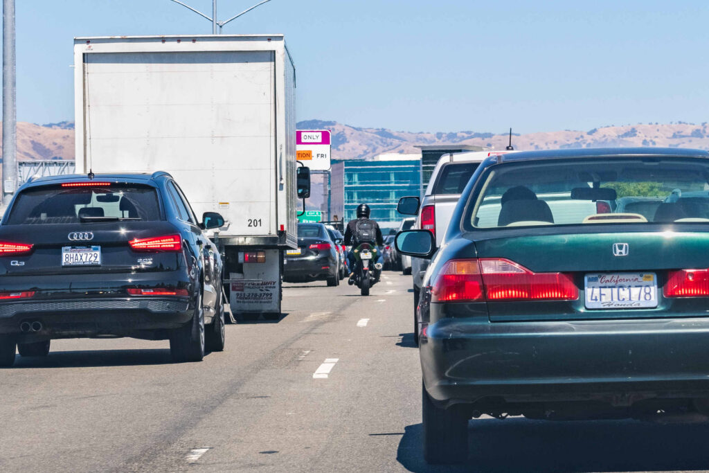A motorcyclist riding between vehicles in heavy traffic illustrates whether Is It Legal to Split Lanes in California.