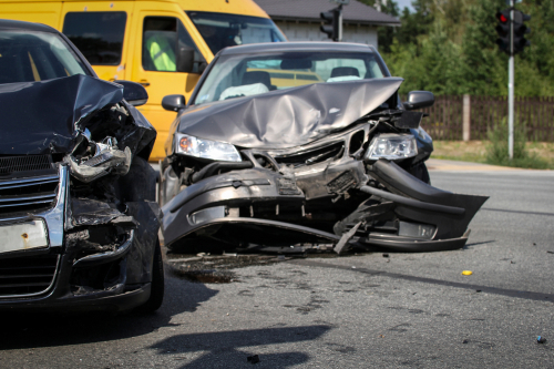 Two heavily damaged cars after a collision at an intersection with a yellow van in the background.