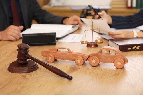Lawyers discussing a car accident case with wooden car models, gavel, and scales of justice on the desk.