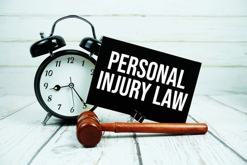 A wooden gavel rests beside a black clock and a sign reading “Personal Injury Law” on a white wooden surface, symbolizing legal deadlines.
