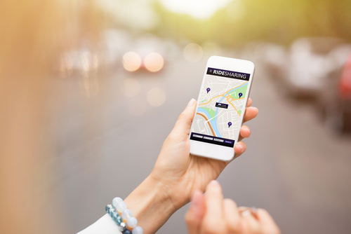 Close-up of a person holding a smartphone with a ridesharing app open showing a city map and pickup points.
