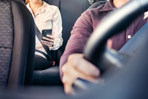 Female passenger in back seat holding phone while rideshare driver focuses on the road.
