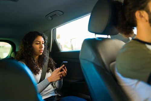Woman sitting in the back seat of a rideshare car using her phone while wearing a seatbelt.