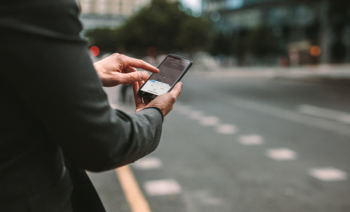 Person using a rideshare app on a smartphone while standing near a city street.
