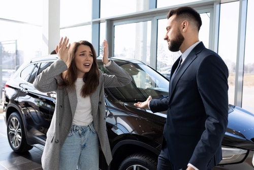 Woman arguing with a car salesman in a showroom next to a black vehicle.