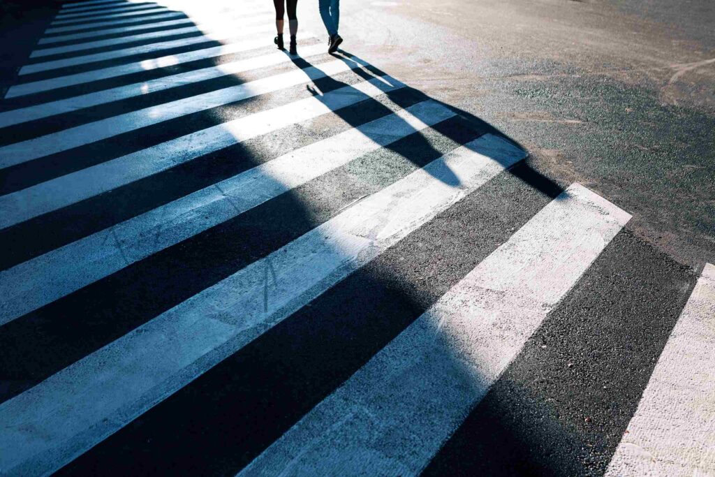 Shadows of two people walking across a marked crosswalk, illustrating pedestrian right-of-way rules in California.