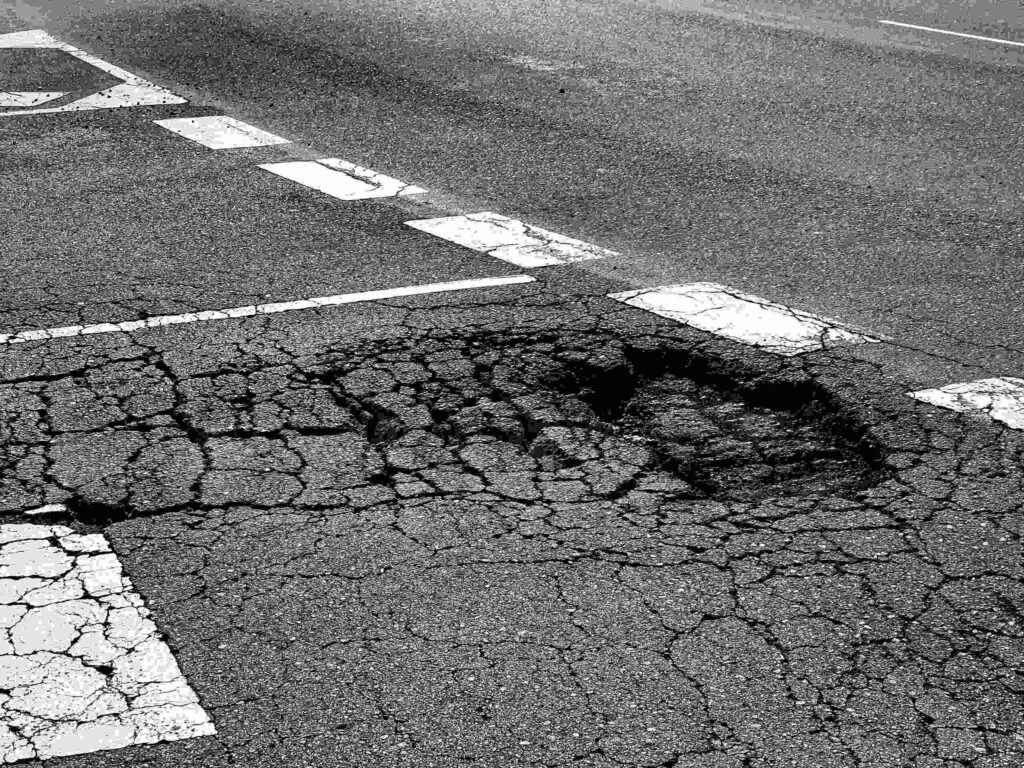 A deep, cracked pothole in a Bakersfield asphalt road, illustrating hazardous conditions that lead to car accidents.