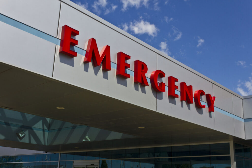 Large, red, three-dimensional letters spelling "EMERGENCY" on the exterior facade of a hospital building under a bright blue sky, representing medical care for victims seeking Bakersfield catastrophic injury lawyers.