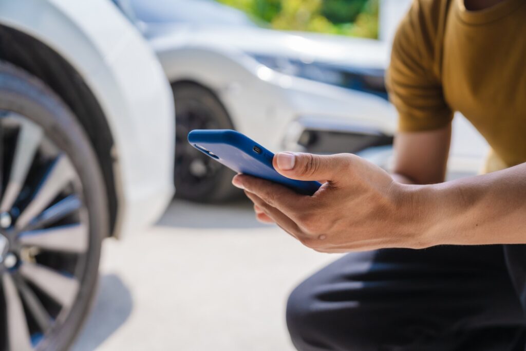 Primer plano de una persona que sostiene un smartphone azul para fotografiar o documentar el lugar de un accidente de tráfico, lo que ilustra la importancia de la recopilación de pruebas, con el apoyo de los abogados especializados en accidentes con fuga de Bakersfield.