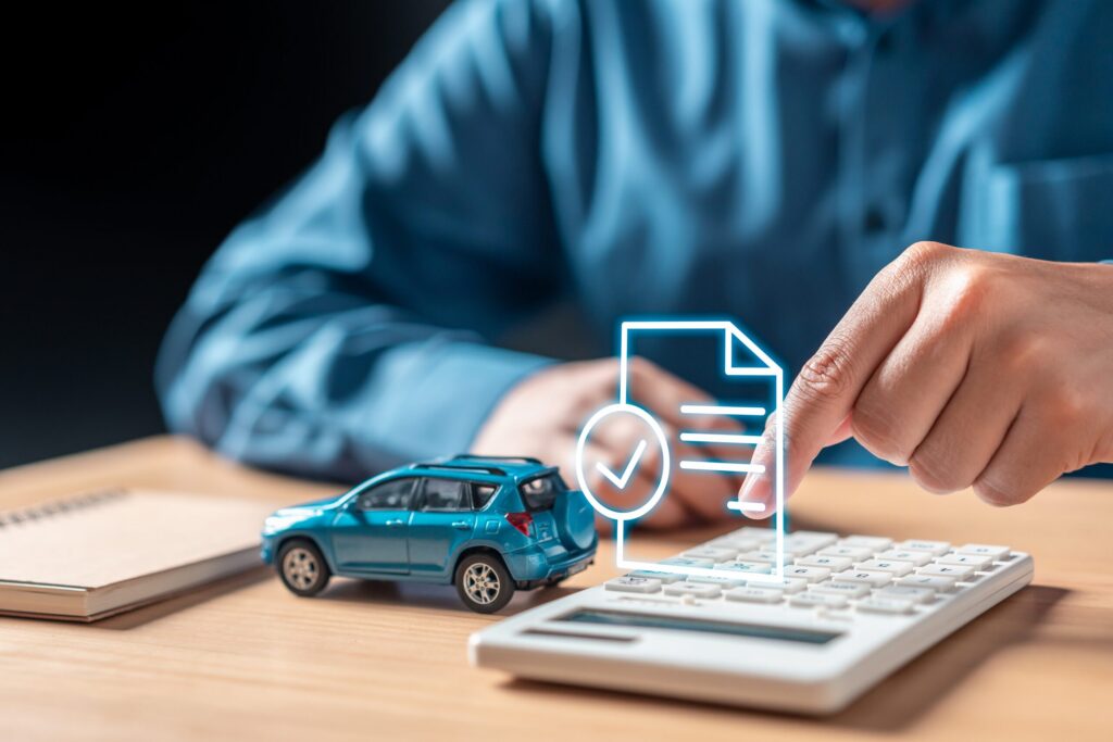 A person points at a calculator next to a small toy car on a wooden desk, featuring a glowing digital insurance document graphic to represent calculations by Bakersfield uninsured/underinsured motorist accident lawyers.