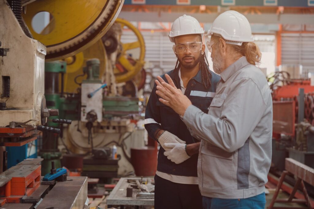 Factory workers discussing heavy machinery operations, representing industrial site claims handled by Bakersfield third-party construction injury lawyers.