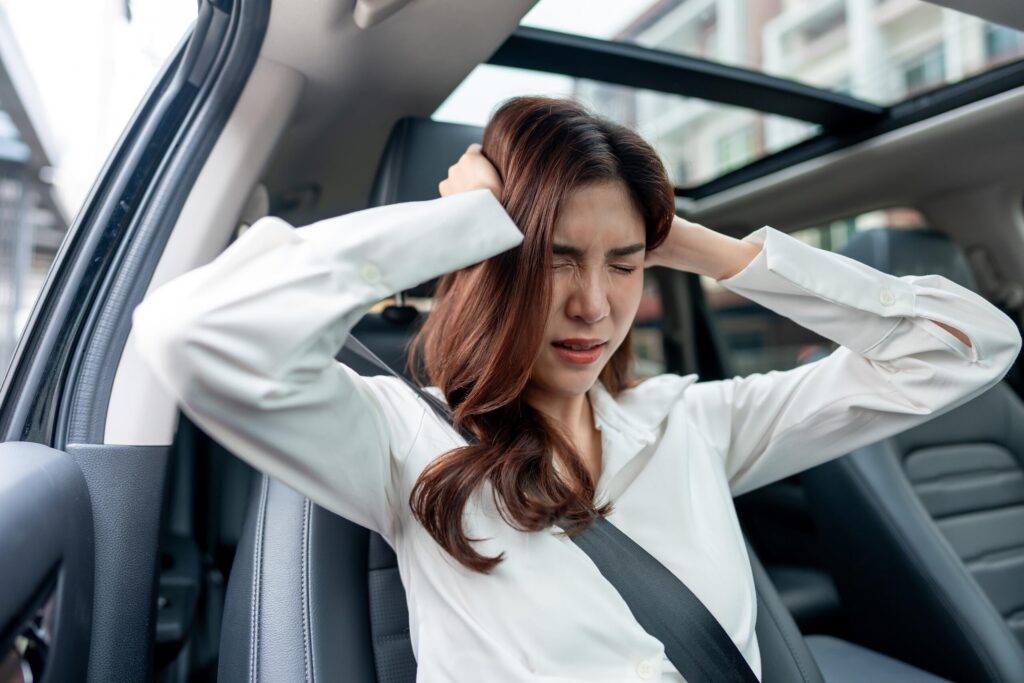A distressed woman holding her head while sitting in a vehicle raises the question can you recover emotional distress damages after a car accident in California.