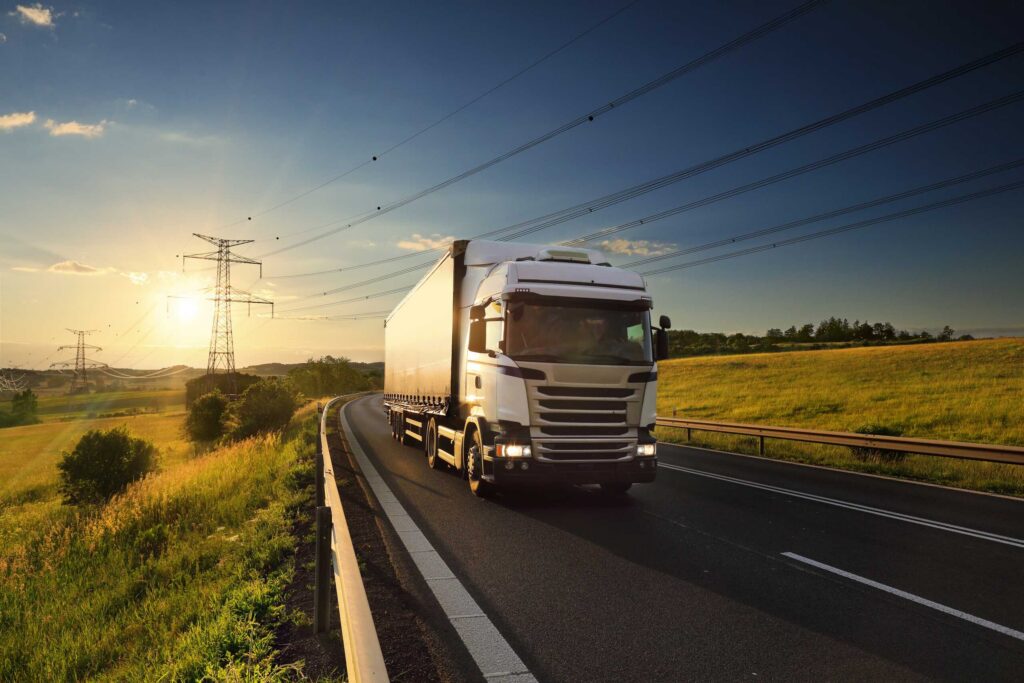 A white commercial truck driving along a two lane highway at sunset illustrates issues around CDL Violations and Driver Qualifications: Negligence in a Bakersfield Truck Accident.
