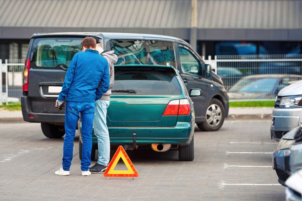 Two drivers inspecting rear bumper damage near a warning triangle highlight determining Who's Liable for a Car Accident in a Bakersfield Parking Lot.