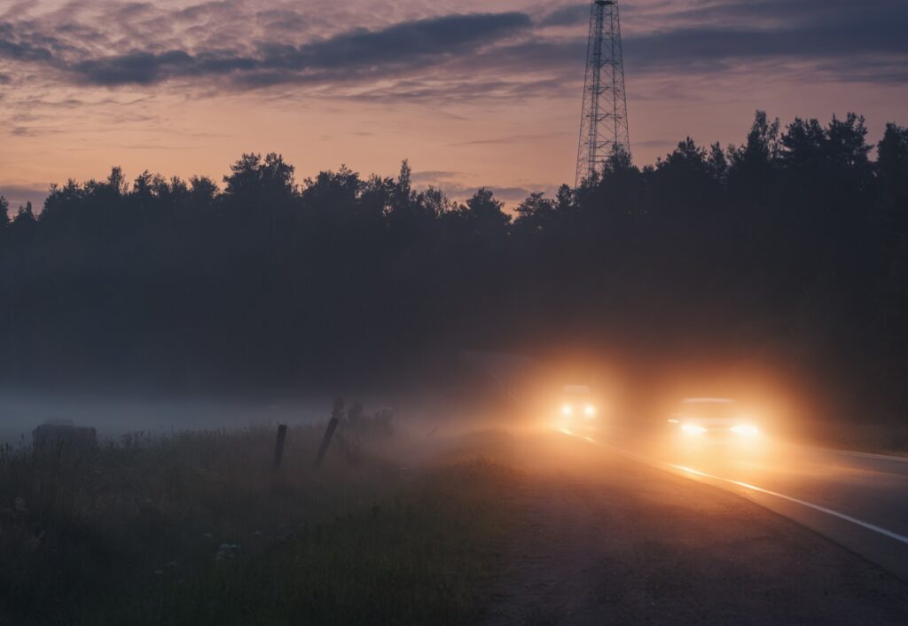 Headlights cutting through thick fog at dusk show dangerous driving conditions related to Tule Fog and Truck Accidents on Highway 99 and I-5 in Kern County.