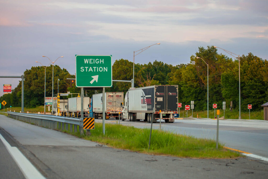 Semi trucks lining up at a highway scale illustrate how inspections prevent Weigh Station Violations in Bakersfield Truck Accidents.