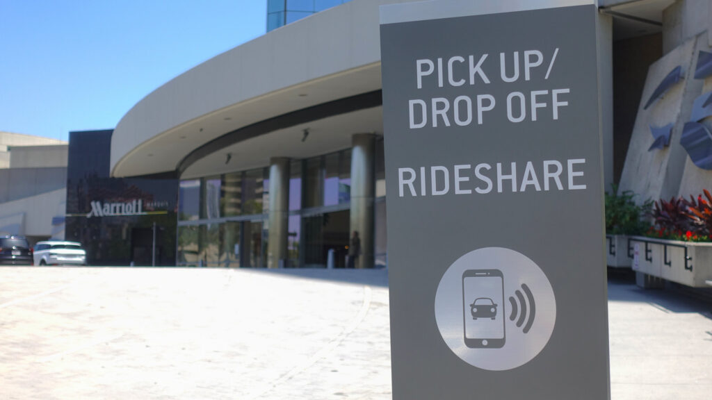 A grey rideshare pickup and drop off sign standing outside a modern building.