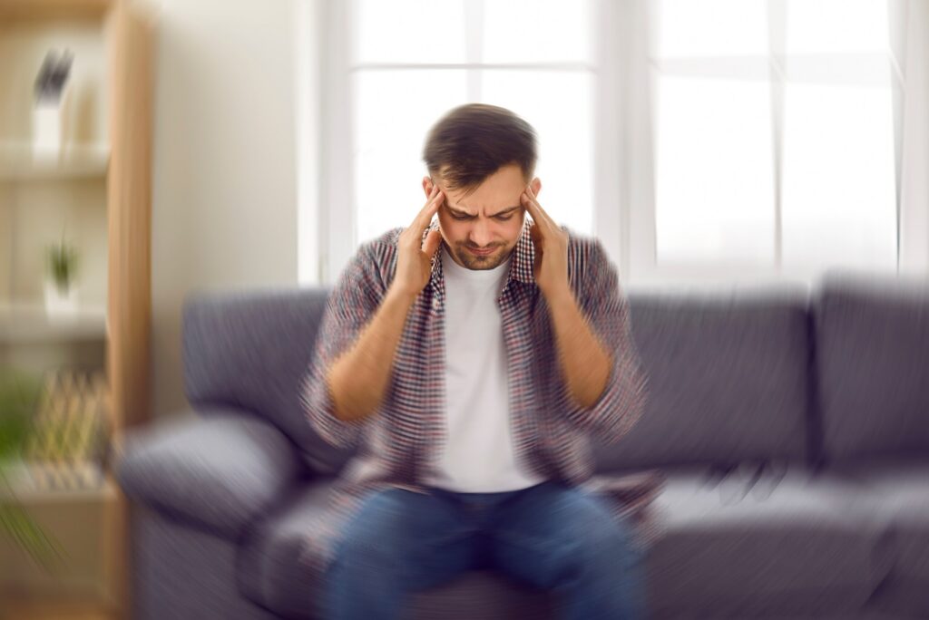 A man sitting on a couch touching his temples while suffering from a severe headache.