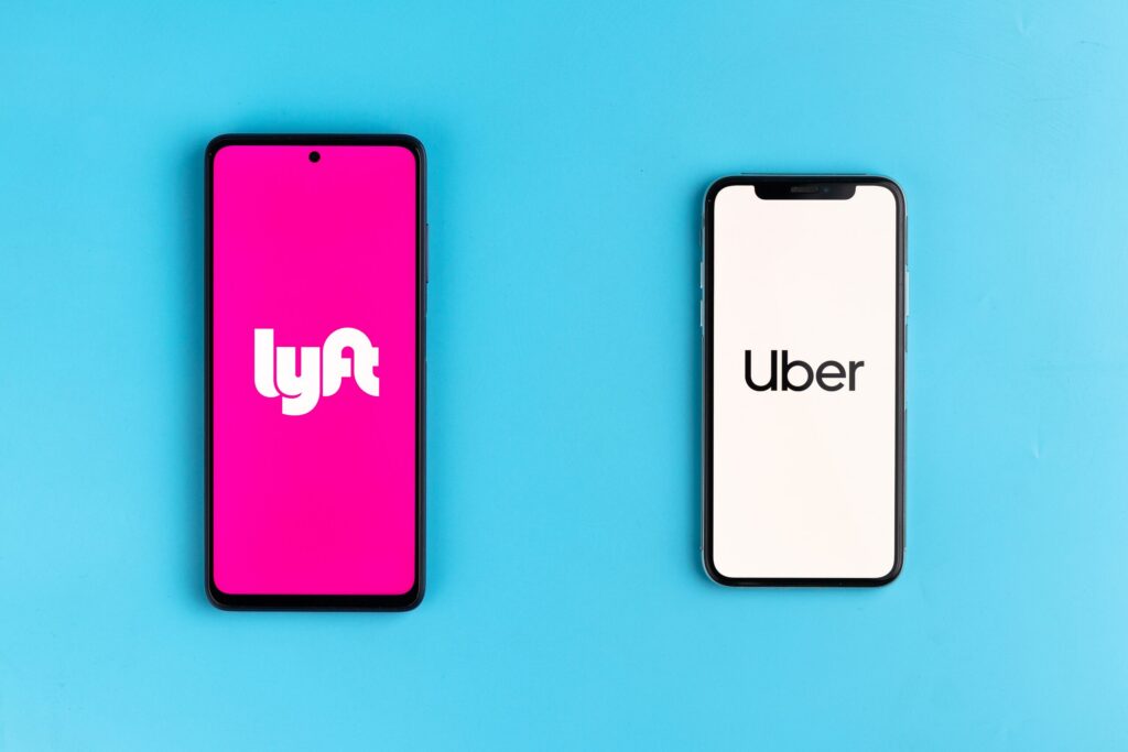 Two smartphones lying side by side displaying the Lyft and Uber app logos on a blue background.