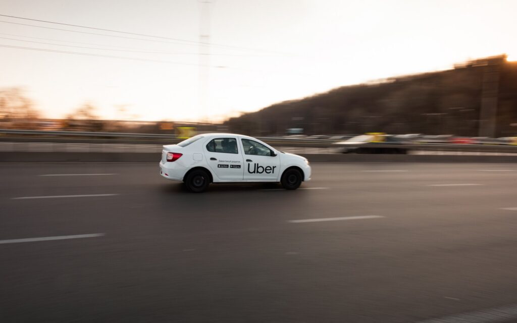 A white Uber car driving along a highway at sunset.